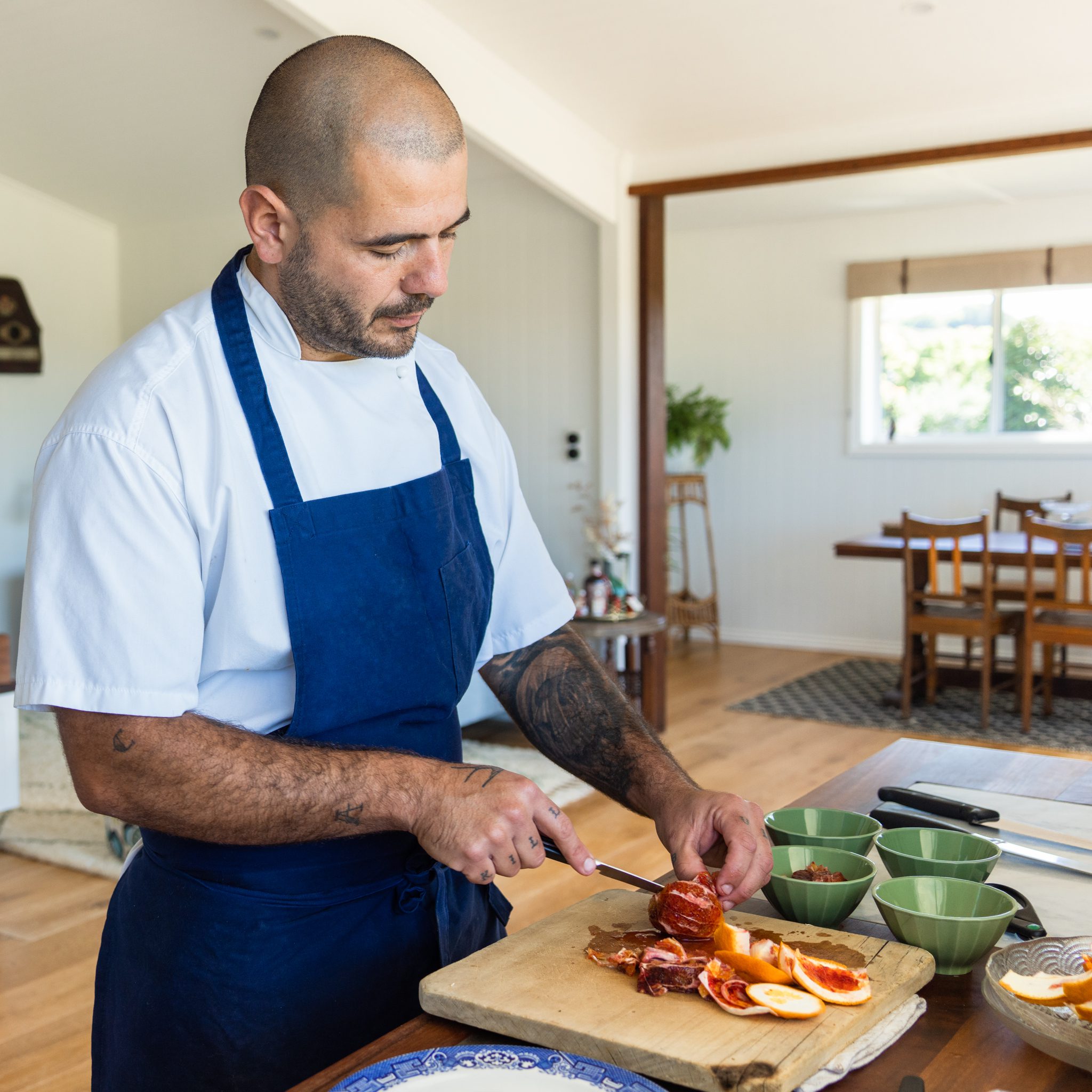 professional chef wearing a blue apron chopping an orange in the heartwood farm cottage kitchen