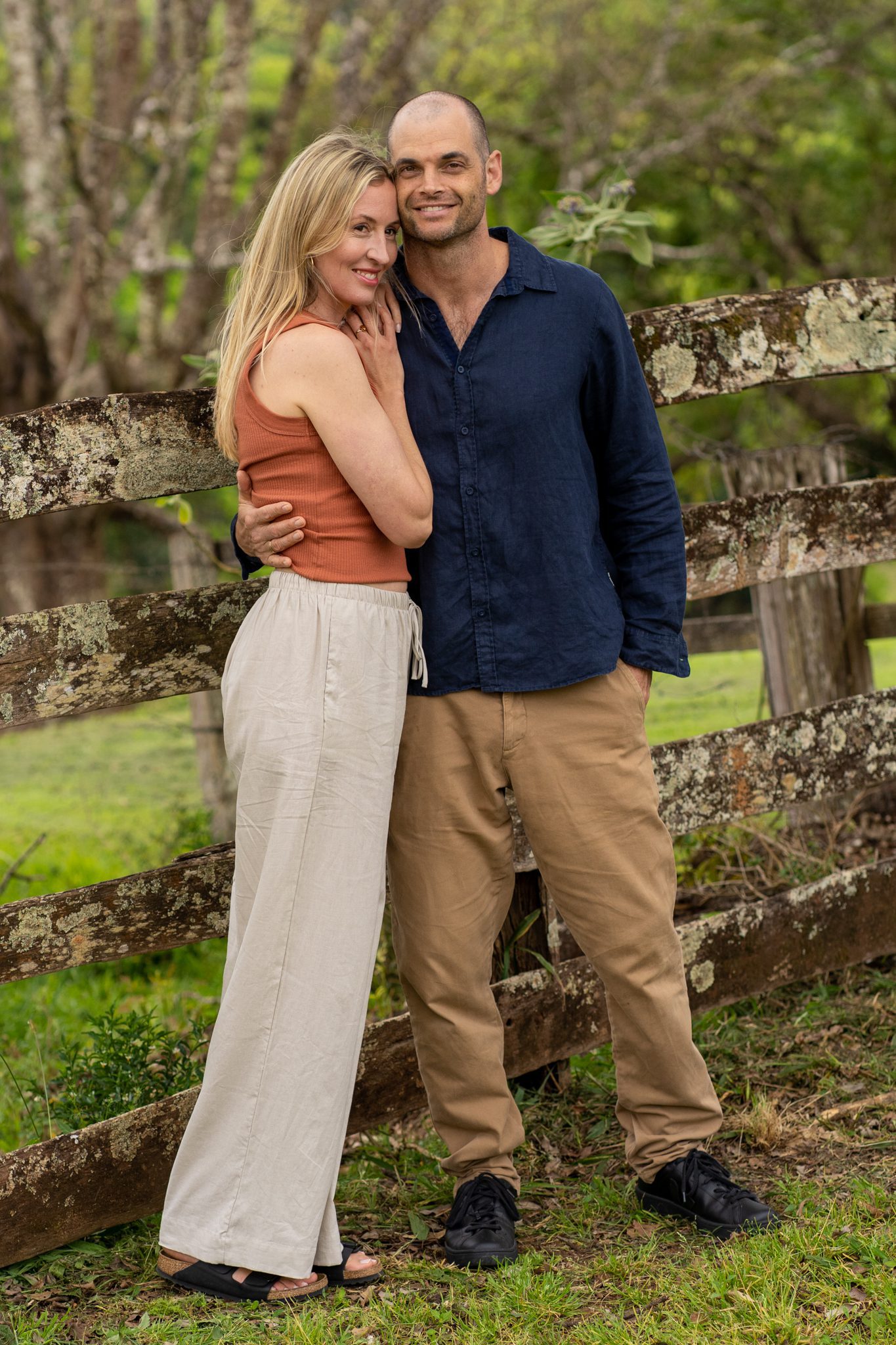 casually dressed man and woman for portrait branding standing close together in front of a old fence at heartwood farm