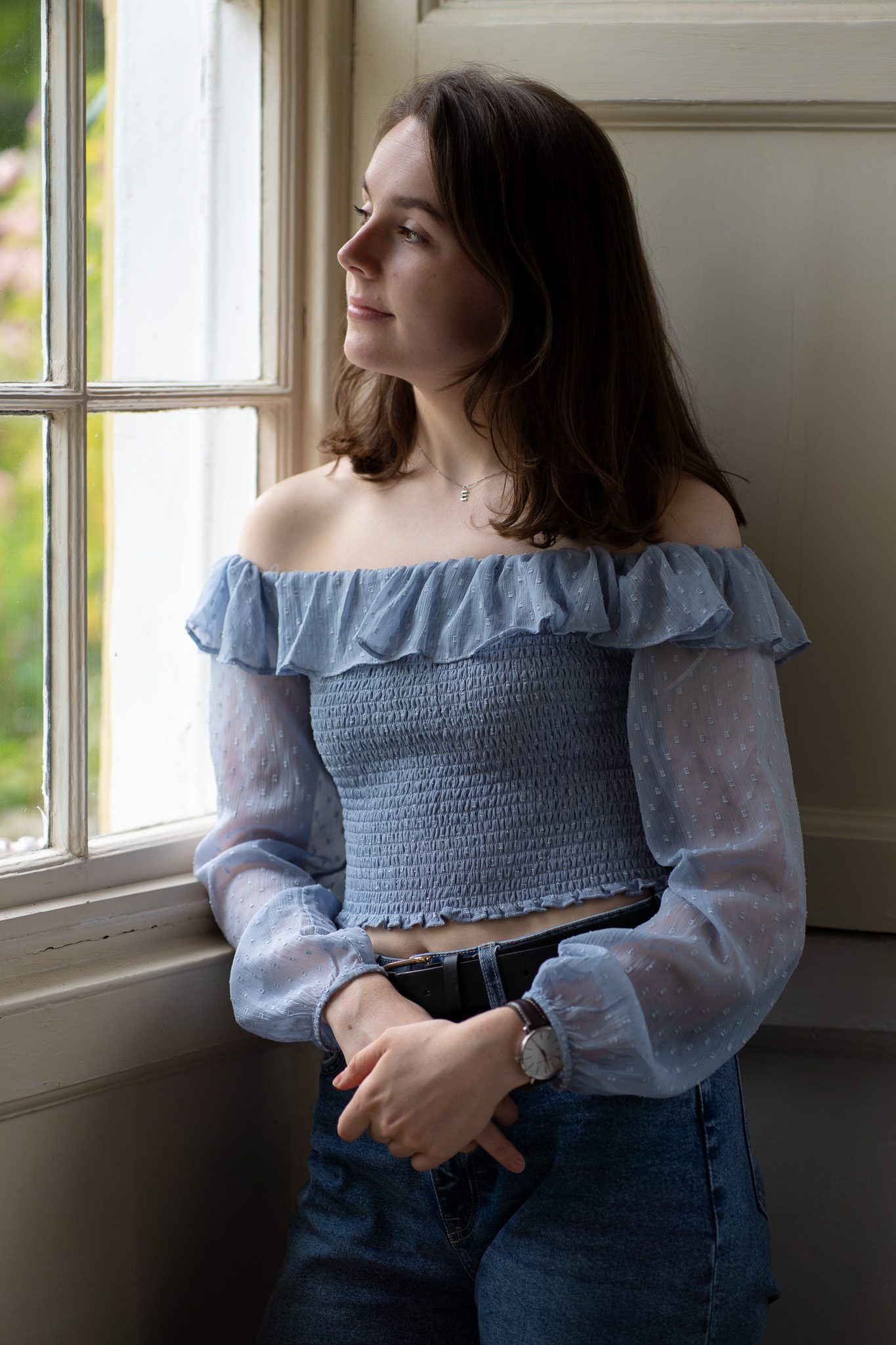 young dark-haired woman looking out of a window wearing a light blue top as she is photographed for the portraits page