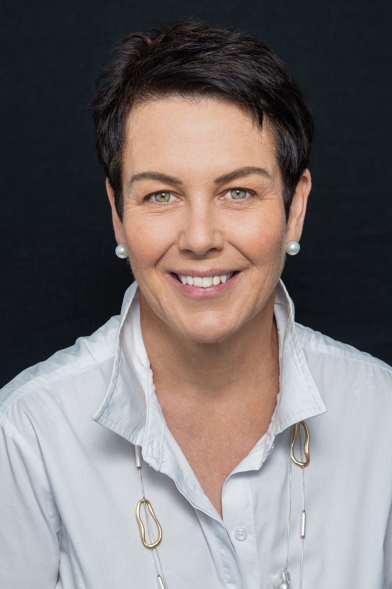dark-haired woman with blue eyes wearing pearl earrings and a white shirt being photographed for the corporate headshots page