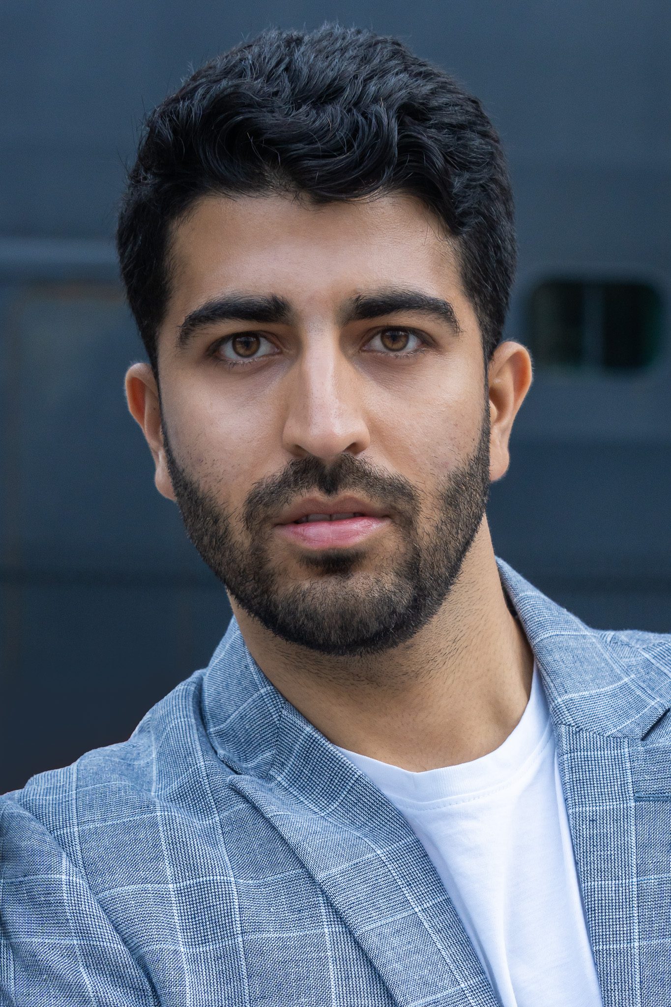 headshot of an Indian male model with brown eyes and a beard wearing a blue checked jacket and white t-shirt being photographed by Georgie Greene Photography for the model portfolios webpage