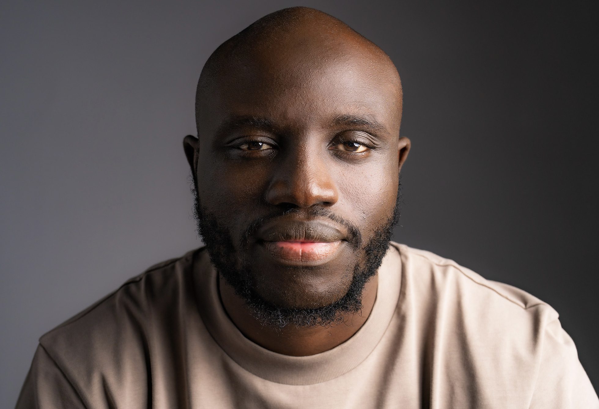 head and shoulders shot of a black bald male model wearing a beard and looking directly into the camera for the portraits webpage
