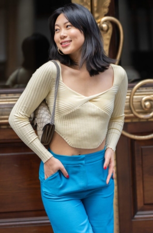 Asian young model wearing blue trousers and carrying a handbag as she poses in front of a doorway while her portraits are being taken