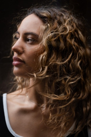 headshot profile of a Model with curly wind-swept hair standing in a dark alleyway as her portraits are being taken