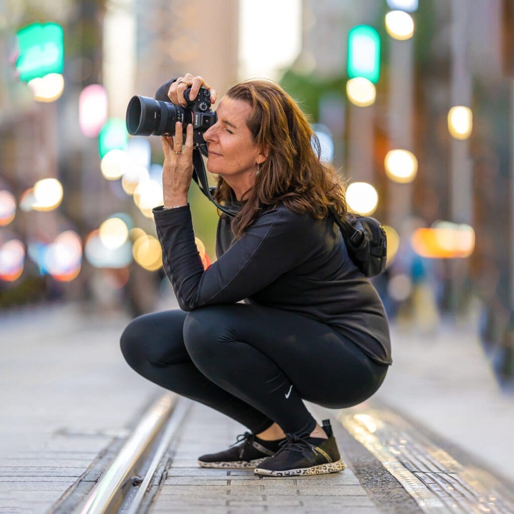 Sydney professional headshots photographer Georgie Greene wearing black and crouching on the tram tracks in Sydney's cbd where she is taking a photograph at the same time her portraits are being taken