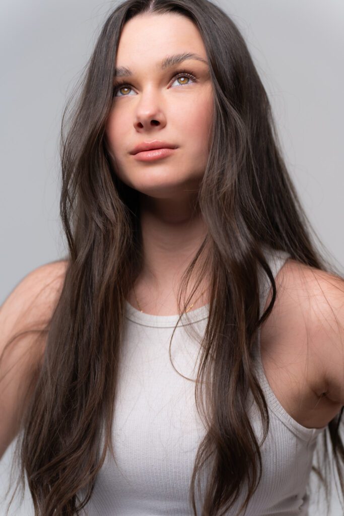 dark haired model with very long hair wearing a white top looking up as her portrait is taken