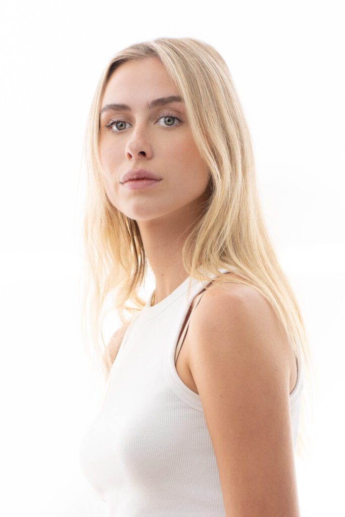 Blonde model wearing white in front of a white background as her portrait is taken