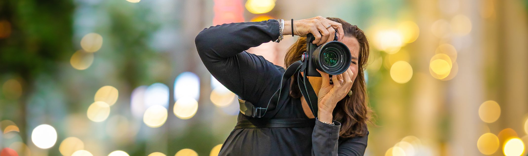 photographer Georgie Greene taking a photograph in a Sydney street with bokeh city lights behind her
