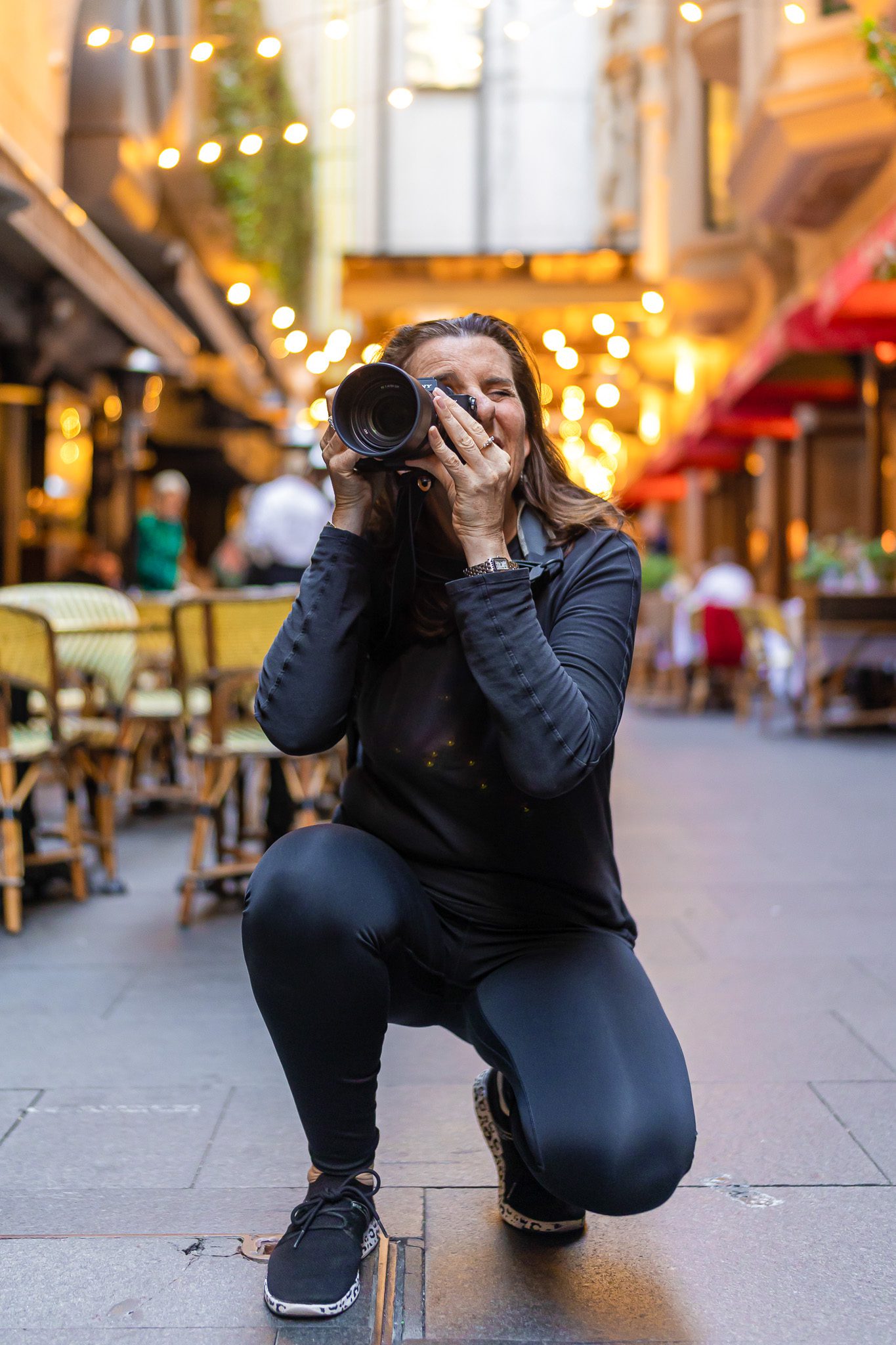 Photographer wearing black and crouching down to take a street scene with bright lights