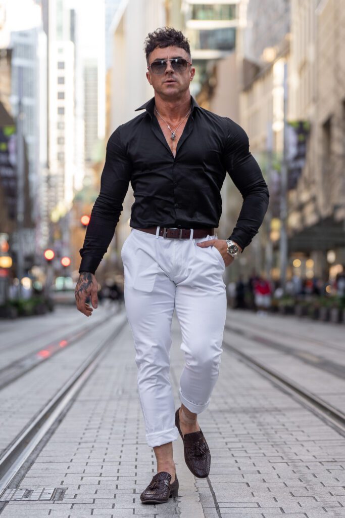 young man wearing sun glasses a black top and white jeans who is walking down the tram tracks while his personal branding portrait is being taken