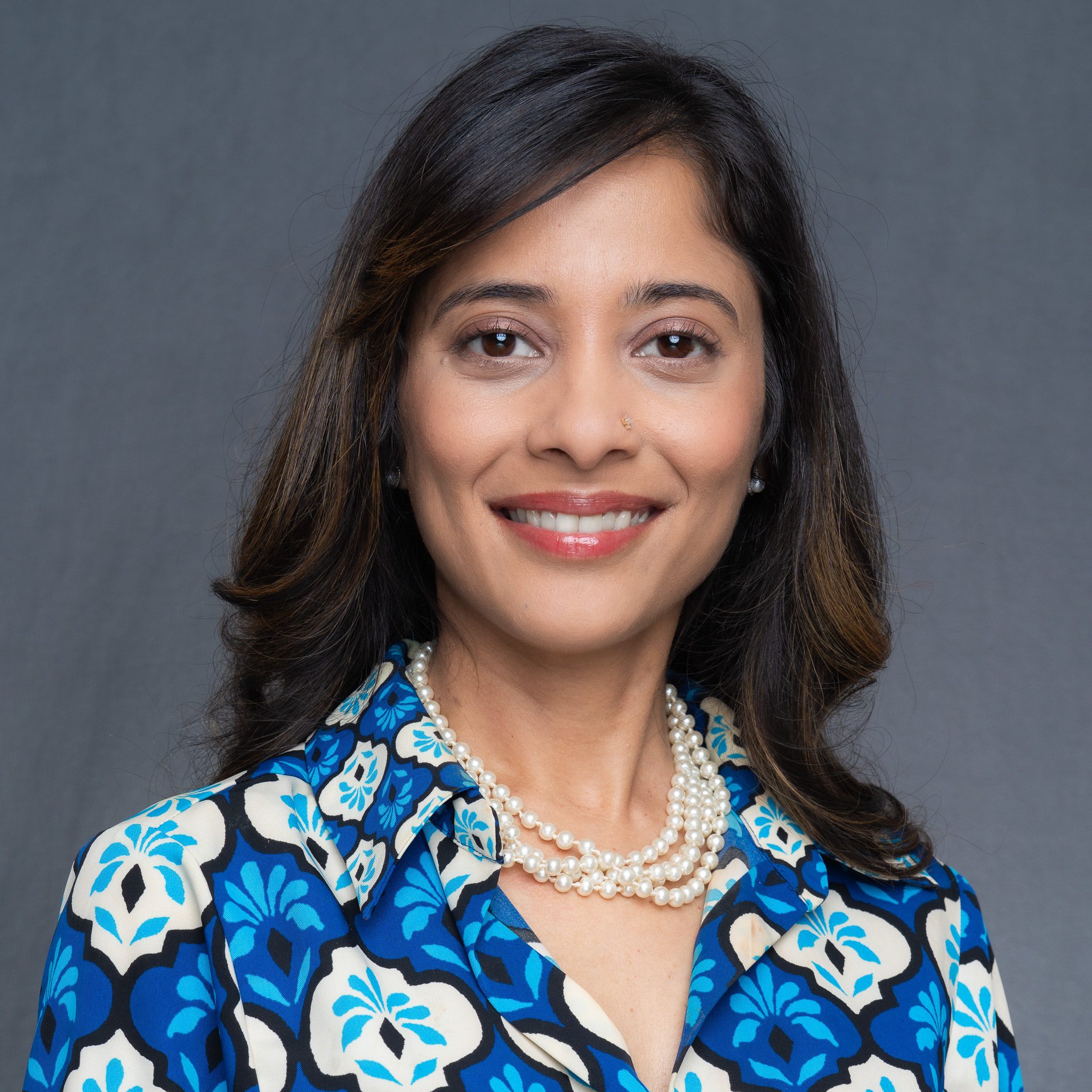 a professional Indian woman with long dark hair and brown eyes wearing a blue and white top and having her corporate headshot taken Georgie Greene Photography