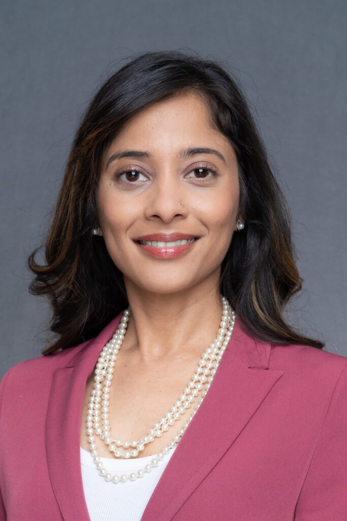 a professional Indian woman with long dark hair and brown eyes wearing a pink top and having her corporate headshot taken
