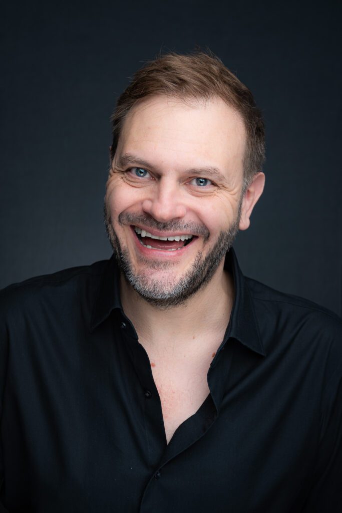 A young smiling man in a black shirt having a headshot taken by Georgie Greene Photography