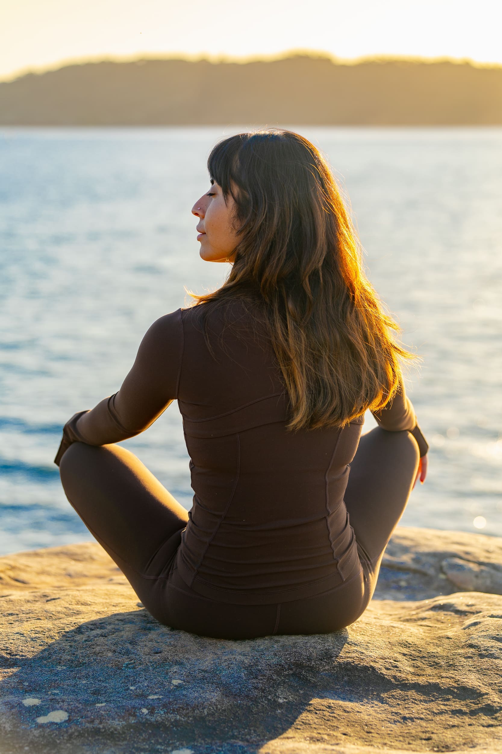 Indian Yoga Teacher wearing brown and meditating on a rock having her personal branding portrait taken by Sydney professional photographer Georgie Greene