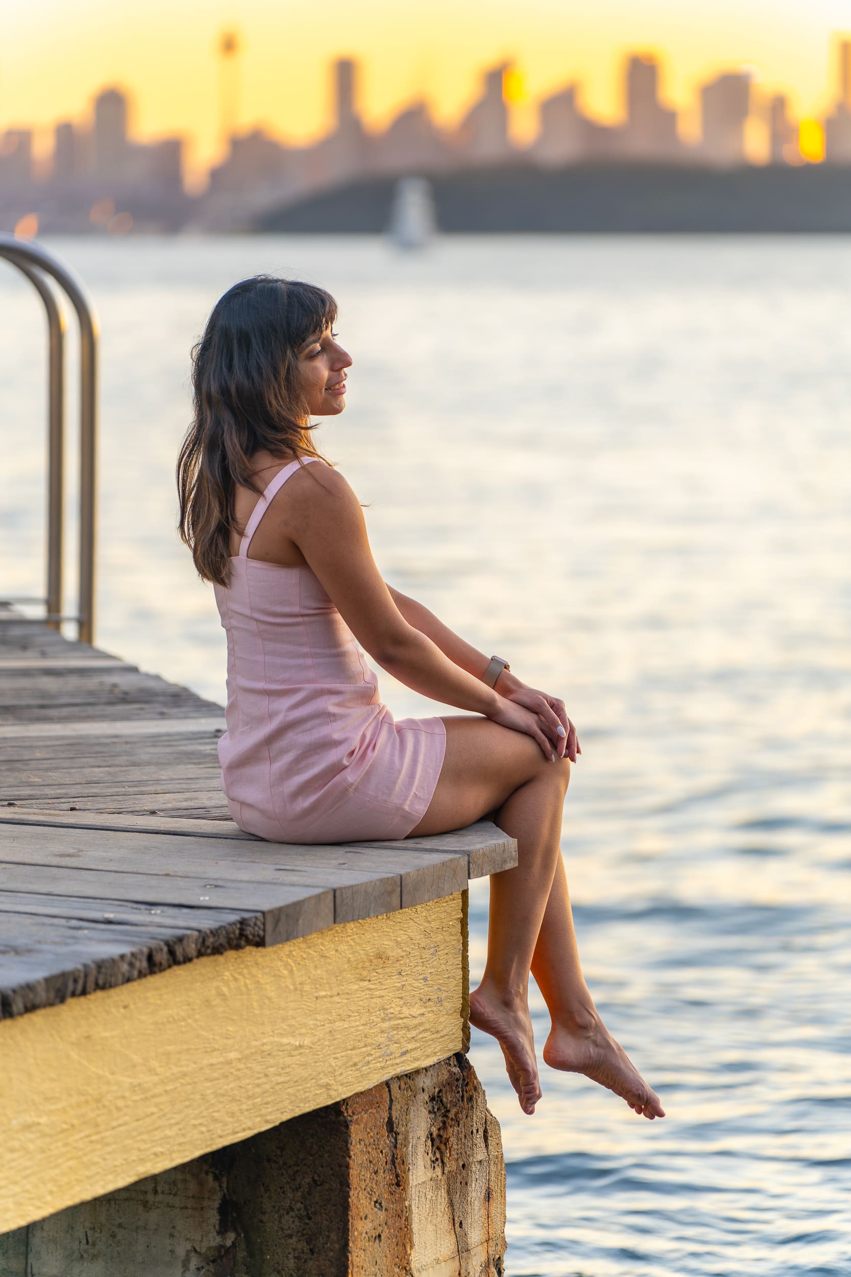 Indian Yoga Teacher wearing pink and sitting on a pier having her personal branding portrait taken by Sydney professional photographer Georgie Greene