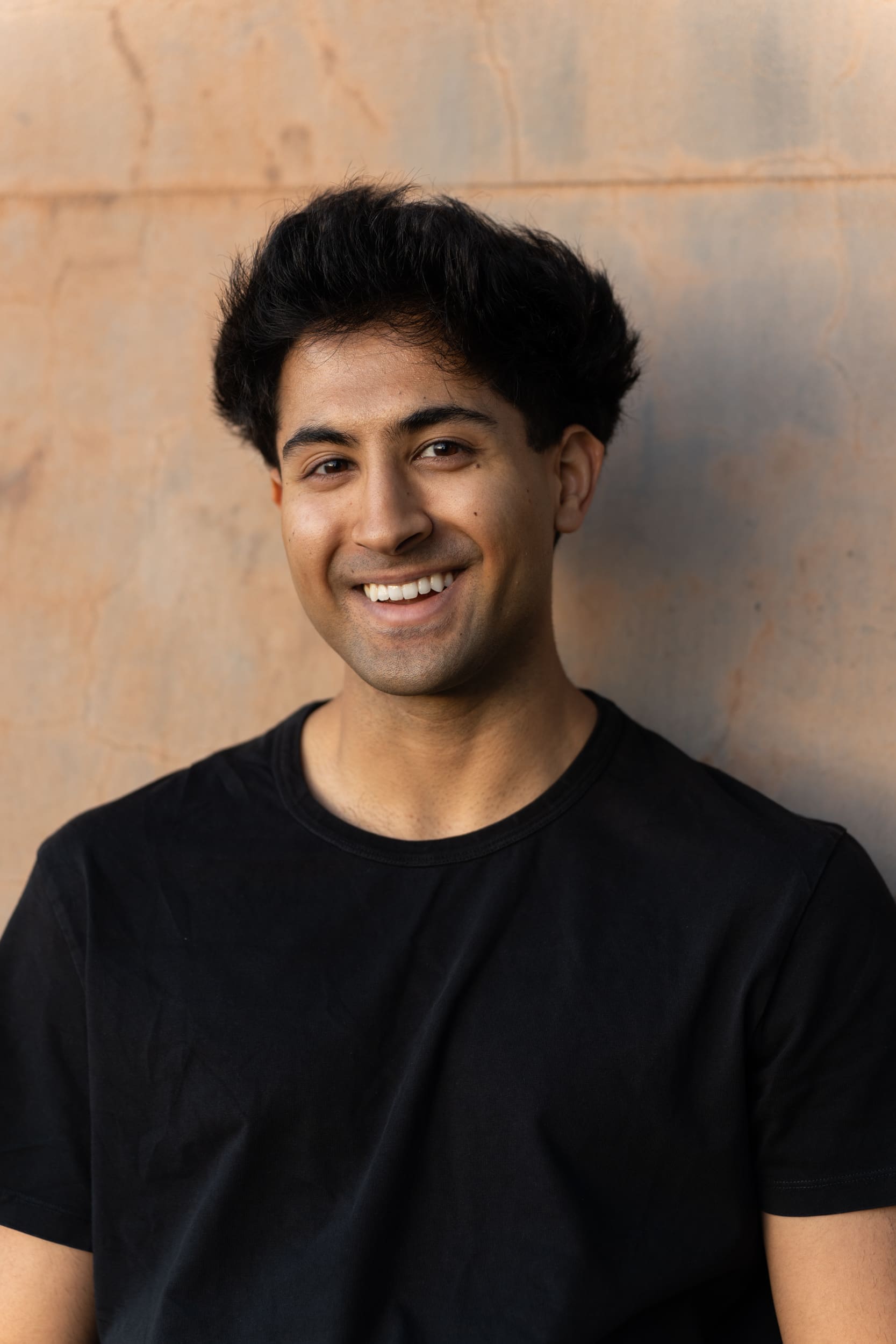 smiling young dark haired man wearing a black t-shirt and standing by a concrete wall having his dating photo taken by Sydney dating photographer Georgie Greene