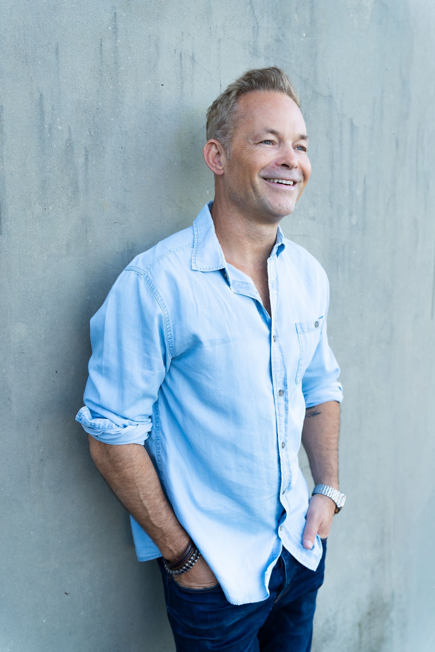 Young blonde haired man wearing a blue denim shirt and standing by a concrete wall having his dating photo taken by Sydney dating photographer Georgie Greene