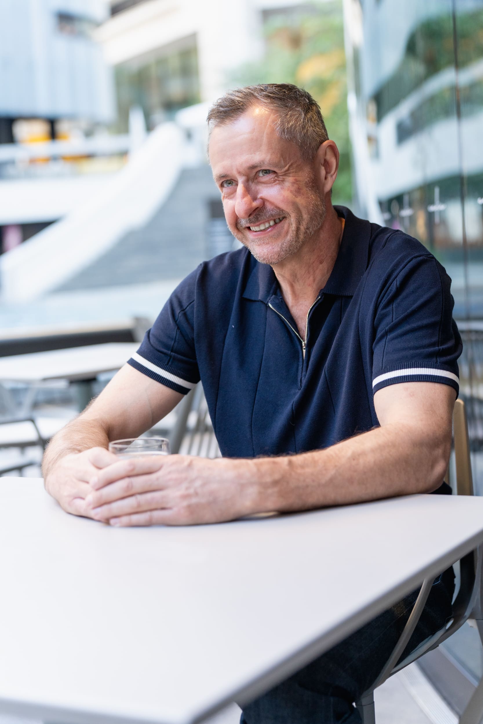 smiling older grey haired man wearing a blue t-shirt and sitting at a cafe table having his dating photo taken by Sydney dating photographer Georgie Greene