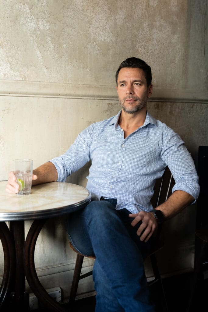 Dark hair man with beard wearing a light blue shirt sitting at a pub table having his dating photo taken by top Sydney dating photographer Georgie Greene