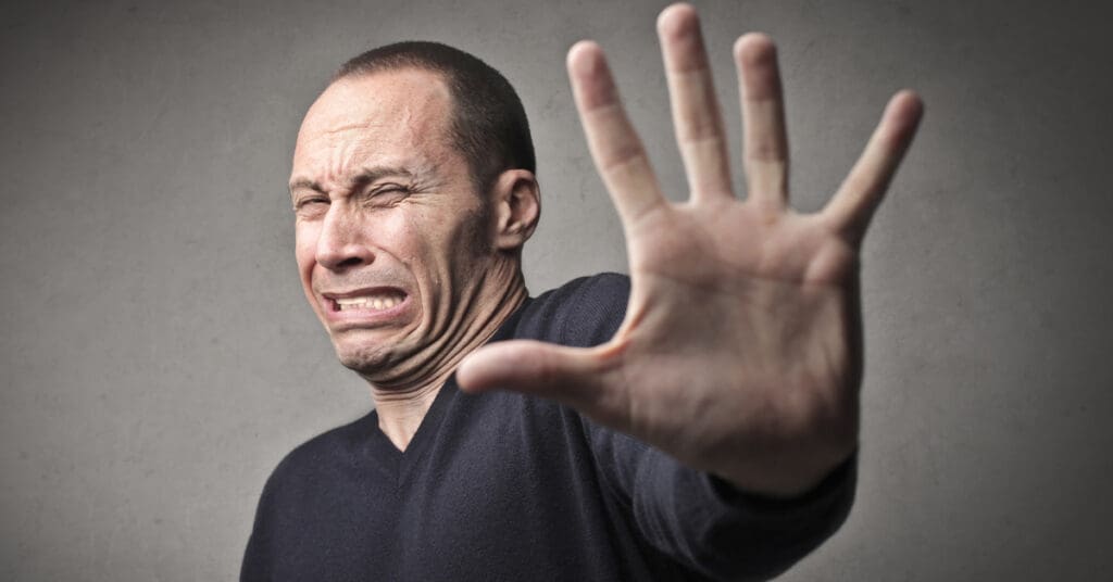Man holding his hand up with a discussed expression on his face as he hates having his photo taken